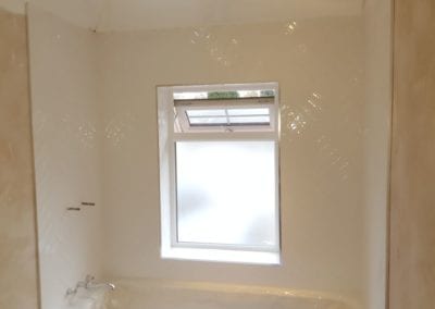 Bathroom wall with a window in the middle surrounded by white gloss tiles